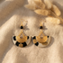 Boucles d'oreilles Ādhā Gōla posées sur un lin naturel, motif léopard en papier lokta résiné, tons ivoire, noir et camel, détails en laiton doré.