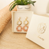 Packaging boucles d'oreilles Nāca fait main, pochette collection papier lokta rose et bronze